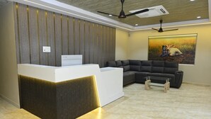 A reception area with a modern reception desk, a sectional sofa, and a painting on the wall. - Anand Vihar Hotel (Ambajipeta)