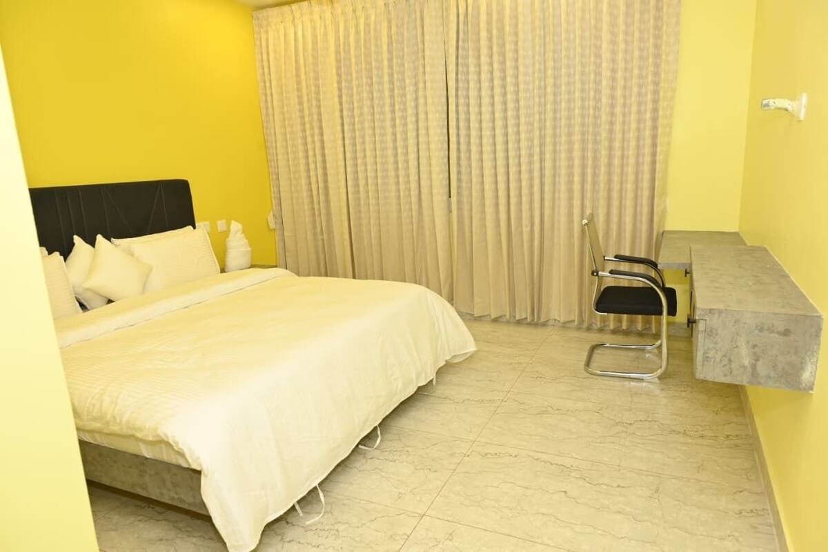 A hotel room with a bed, a chair, a small table, and curtains.