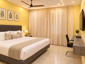 A hotel room with a bed, bedside table, lamp, curtains, and a television. - Anand Vihar Hotel (Ambajipeta)