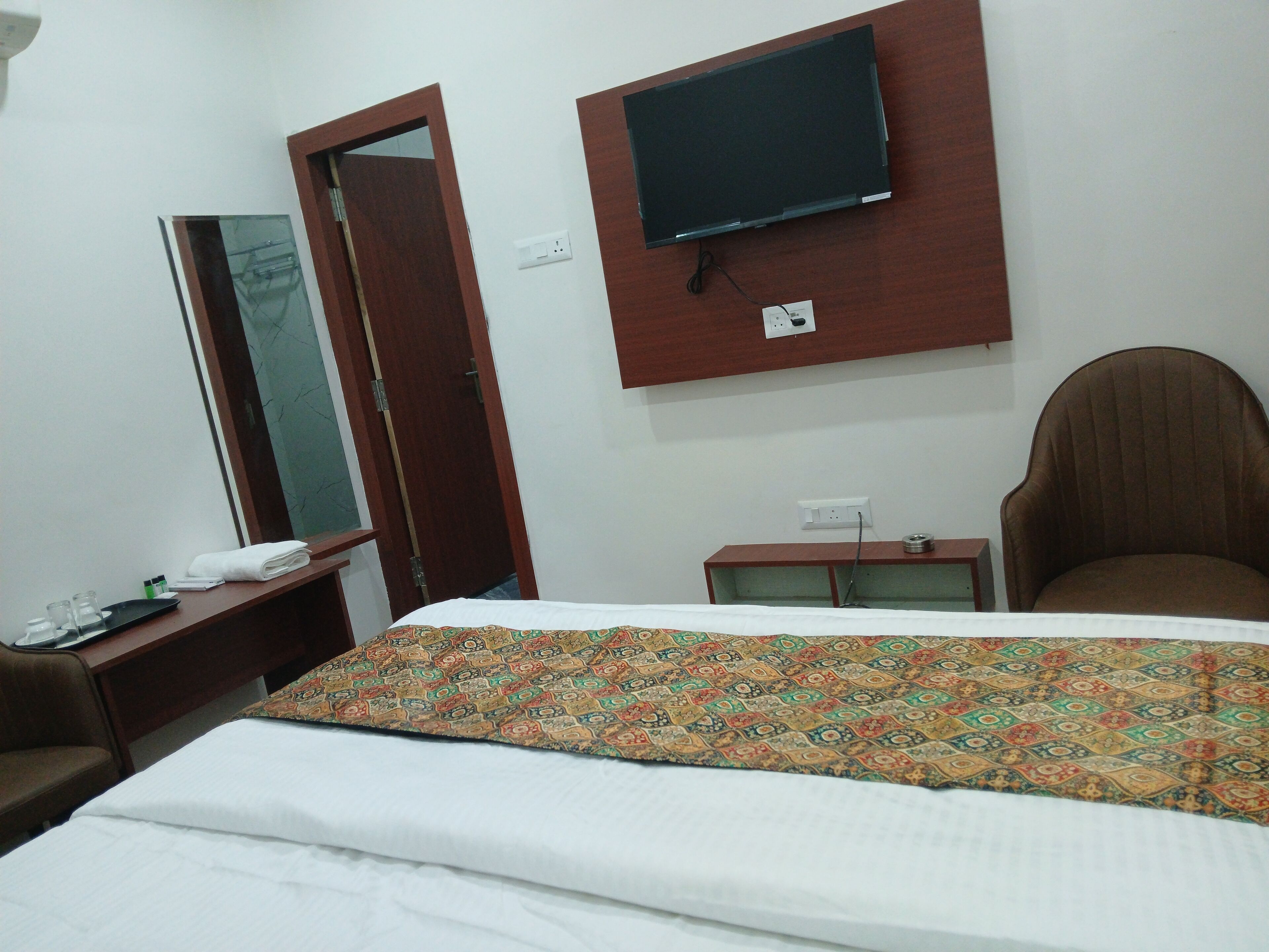 A hotel room with a bed, a television mounted on the wall, a desk with a telephone, and a chair.