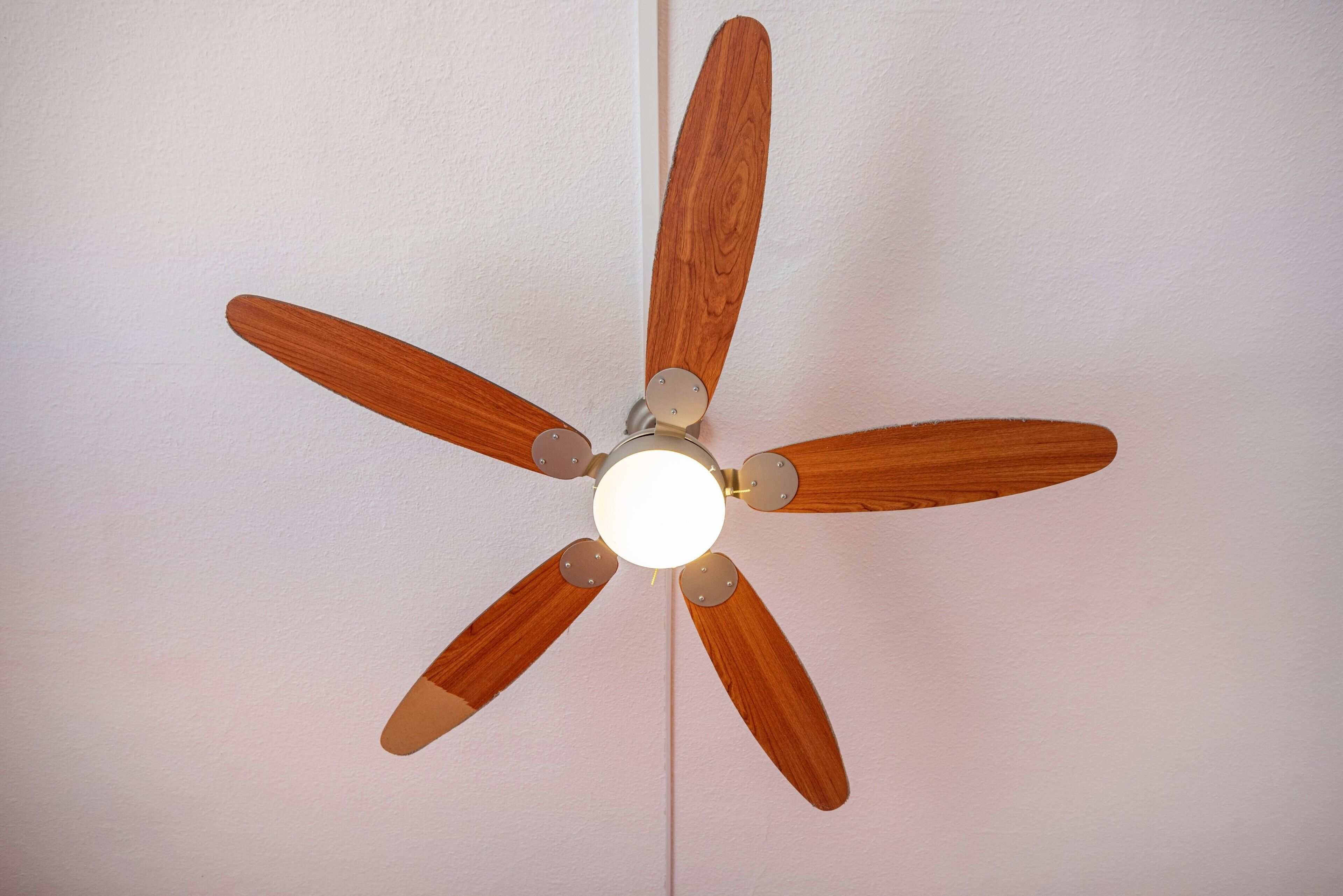 Un ventilador de techo con aspas de madera y una lámpara central.