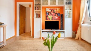 Ein Wohnzimmer mit Fernseher, einer Bücherwand und einem Fenster mit Vorhängen.