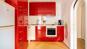 Eine kleine Küche mit roten Schränken, einem weißen Kühlschrank und einem kleinen Backofen.