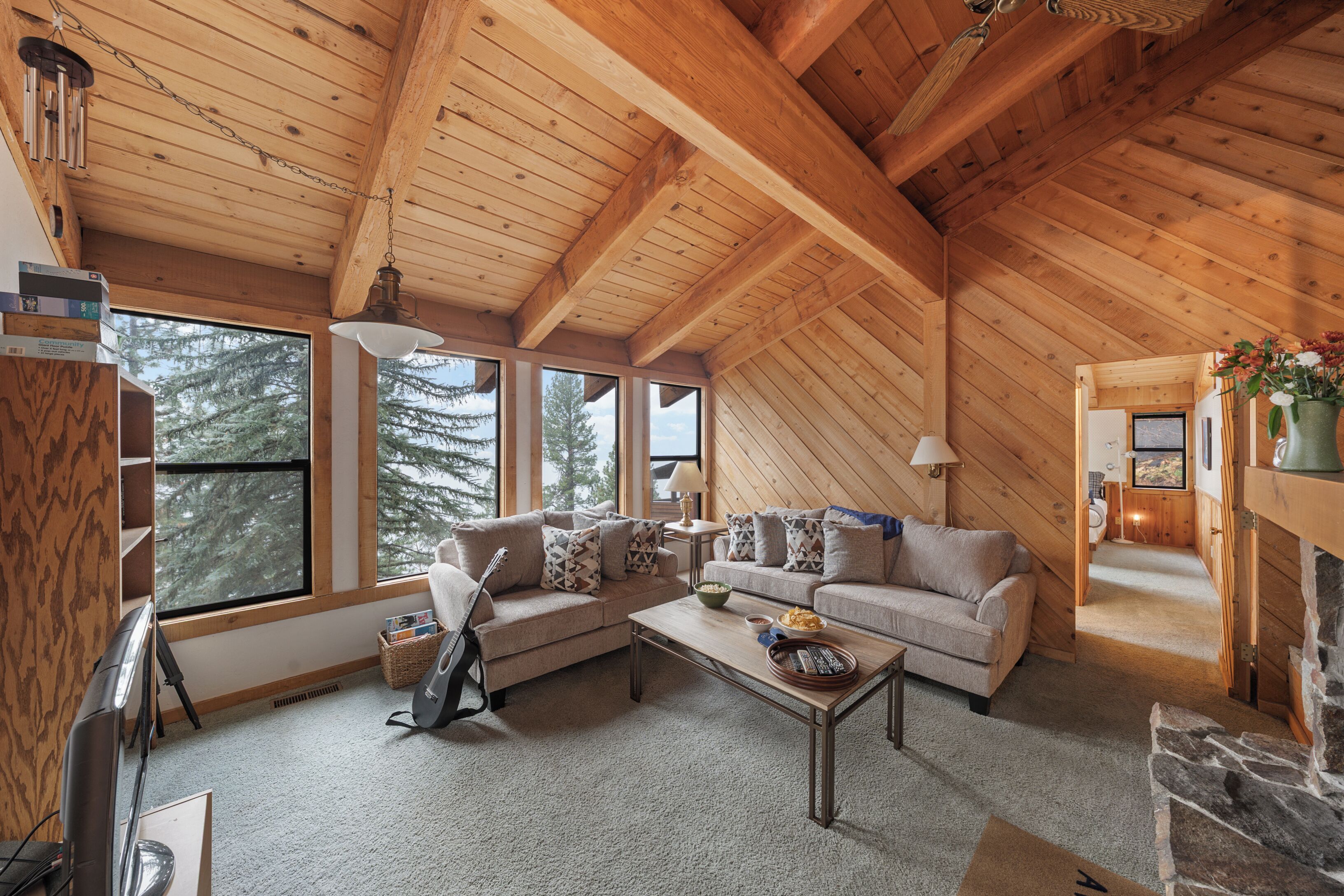 Un salón acogedor con techo de madera, ventanas amplias, chimenea y un conjunto de sofás.