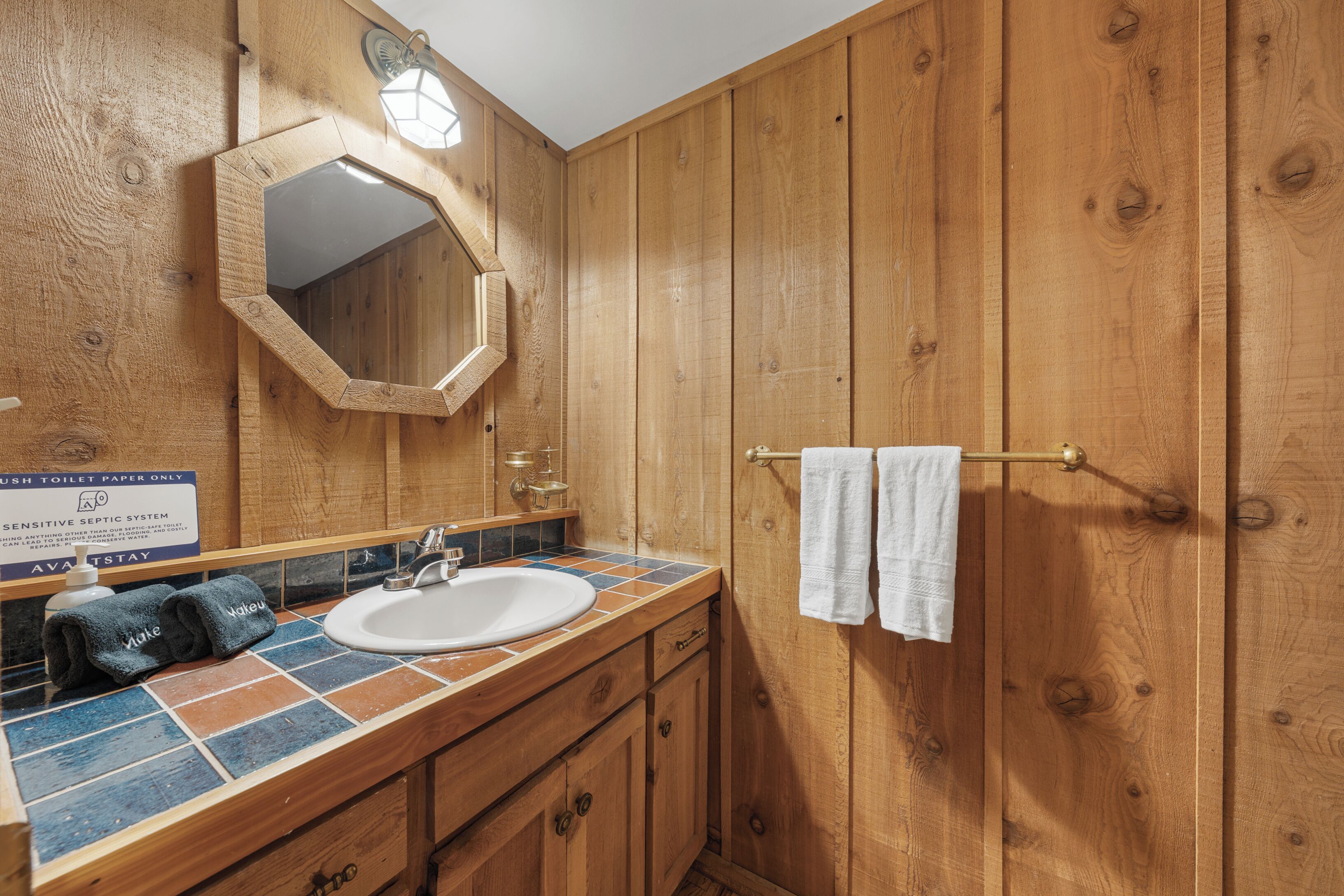 Une salle de bain en bois avec un lavabo blanc, un miroir et un porte-serviettes.