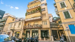 Ένα πολυώροφο κτίριο με μπαλκόνια, είσοδο στο ισόγειο και σταθμευμένες μοτοσικλέτες.