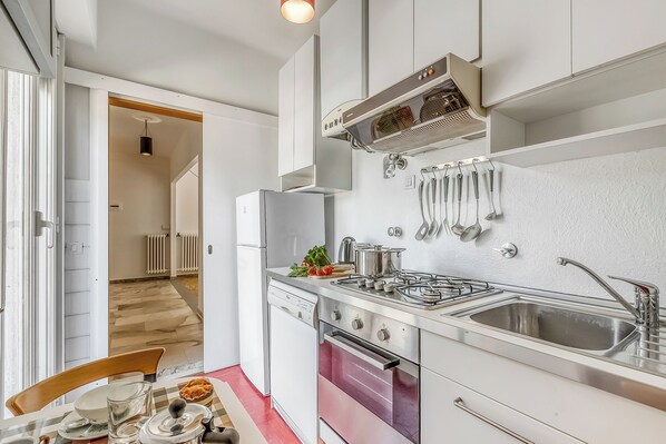 Une cuisine moderne avec des meubles blancs, des appareils en acier inoxydable et un four rouge.