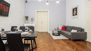 A modern living room with a dining area, a grey sofa, and a flat-screen TV mounted on a white brick wall. - Lumina bright apart near the city center (Łódź)