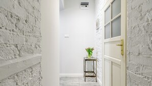 A narrow hallway with white brick walls, a white door with a gold handle, and a small table with a vase of flowers. - Lumina bright apart near the city center (Łódź)