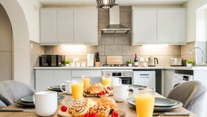 Eine moderne Küche mit weißen Schränken, einem Holztisch mit Frühstücksgebäck und einer Kaffeemaschine.