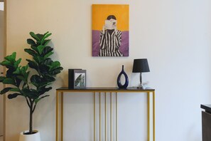 Ein Zimmer mit einer Konsole, einem Blumentopf, einem gerahmten Bild und einem Gemälde an der Wand.