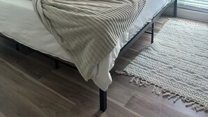 En snyggt bäddad säng med ett vitt täcke och en grön pläd, en tavla som hänger på väggen och föreställer en brygga, en vägglampa och en skylt med texten: ”Vårt hem är fyllt av kärlek”.