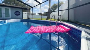 En pool med en rosa, uppblåsbar badleksak, en darttavla och ett avskärmat område med en dörr och fönster.