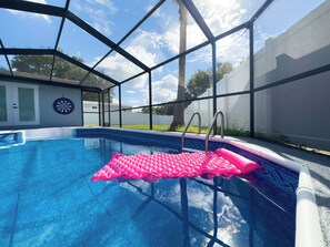 Ein Swimmingpool mit einem rosa Schwimmreifen, einer Dartscheibe und einem überdachten Bereich mit Tür und Fenstern.