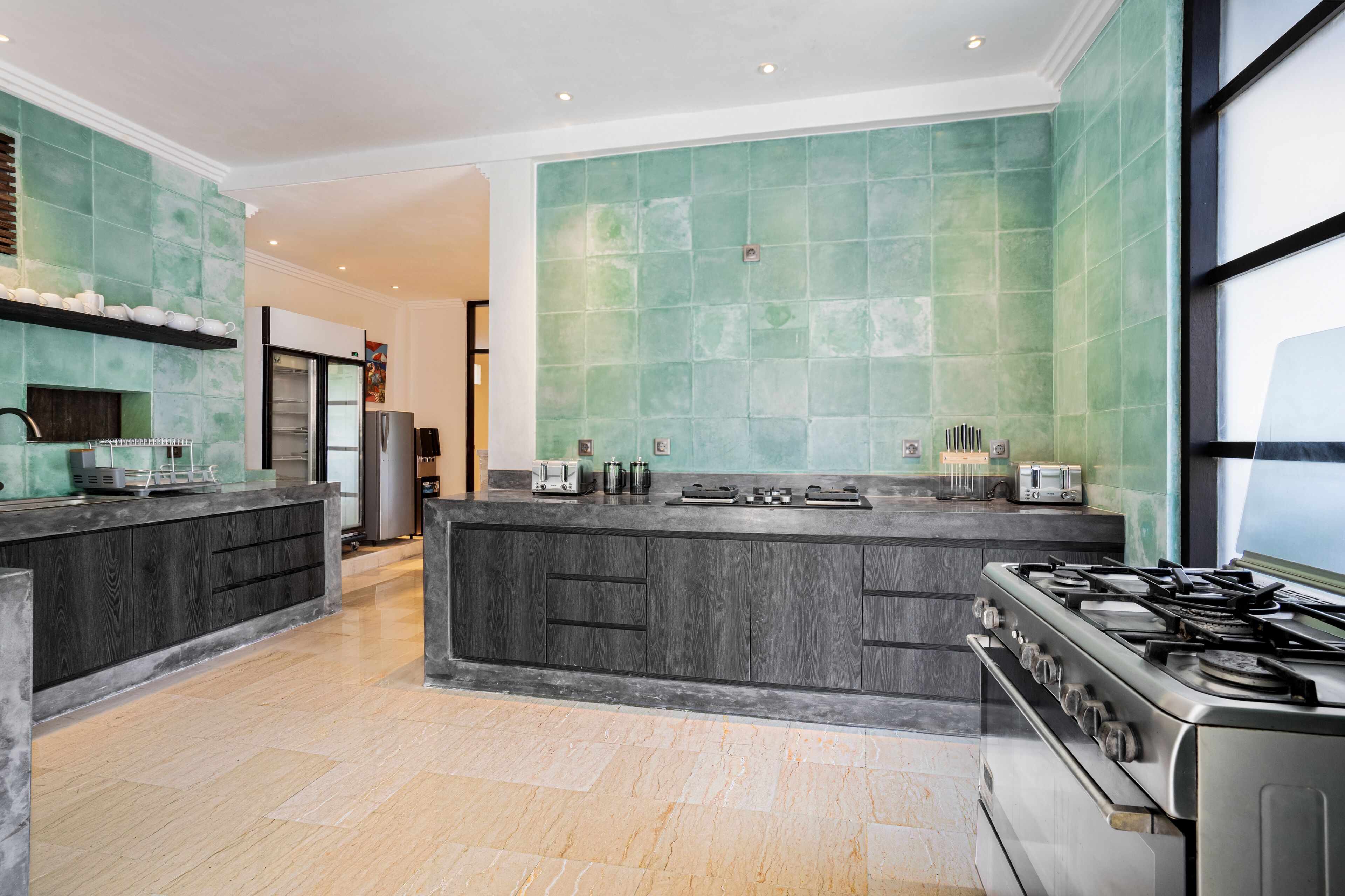 Een moderne keuken met een centraal eiland, roestvrijstalen apparatuur en een groene tegelachtergrond.
