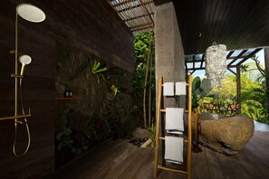 A wooden shower with a gold fixture, a stone wall with greenery, and a wooden ladder with towels. - Le Sunset by Nakula (Ubud)