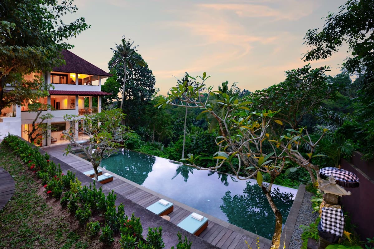 A two-story house with a swimming pool, surrounded by lush greenery.