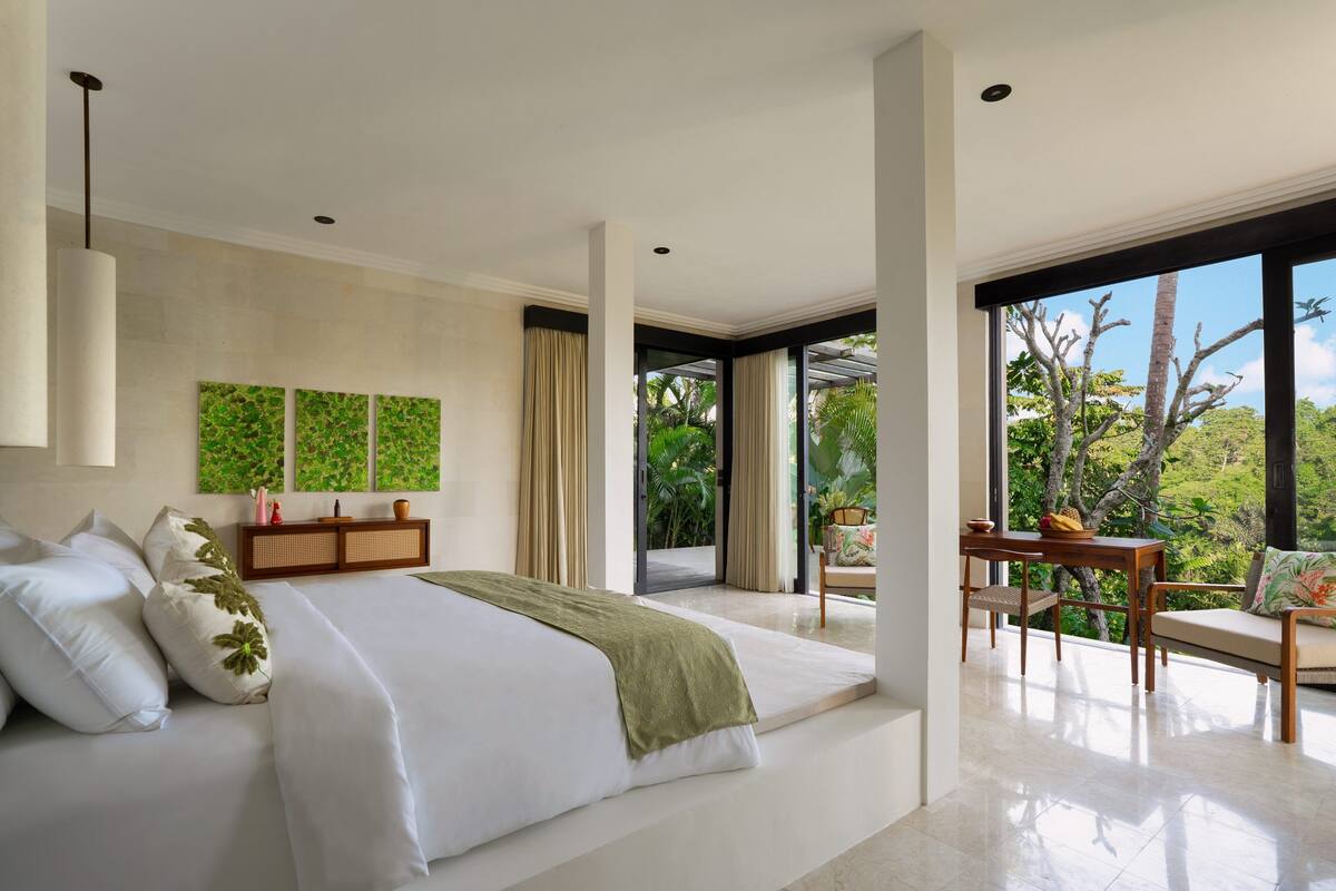A modern bedroom with a large bed, a wooden nightstand, and a view of the outdoors.