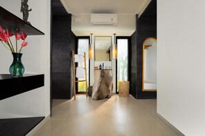 A modern hallway with a stone wall, a wooden stool, and a mirror. - Le Sunset by Nakula (Ubud)