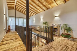 A spacious loft with a high ceiling, wooden beams, a staircase with a metal railing, and a view of a balcony with a railing. - Apartment in a fantastic location surrounded by greenery on our organic apple farm (Partschins)