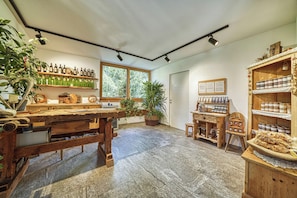 Un intérieur rustique avec des meubles en bois, des étagères remplies de bouteilles et de bocaux, une grande fenêtre et des plantes en pot.