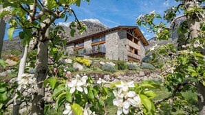 A stone house with a wooden balcony, surrounded by mountains and flowering plants. - Apartment in a fantastic location surrounded by greenery on our organic apple farm (Partschins)