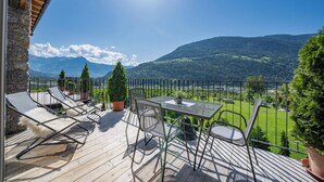 A wooden deck with outdoor furniture, a table, and chairs, overlooking a mountainous landscape. - Apartment in a fantastic location surrounded by greenery on our organic apple farm (Partschins)