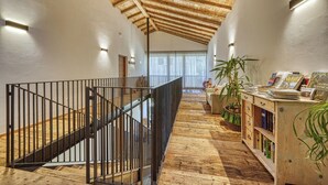 A spacious hallway with a wooden ceiling, a staircase with metal railings, and a wooden bookshelf filled with books. - Apartment in a fantastic location surrounded by greenery on our organic apple farm (Partschins)