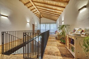 Un hall spacieux avec un plafond en bois, un escalier doté de rampes en métal et une bibliothèque en bois remplie de livres.