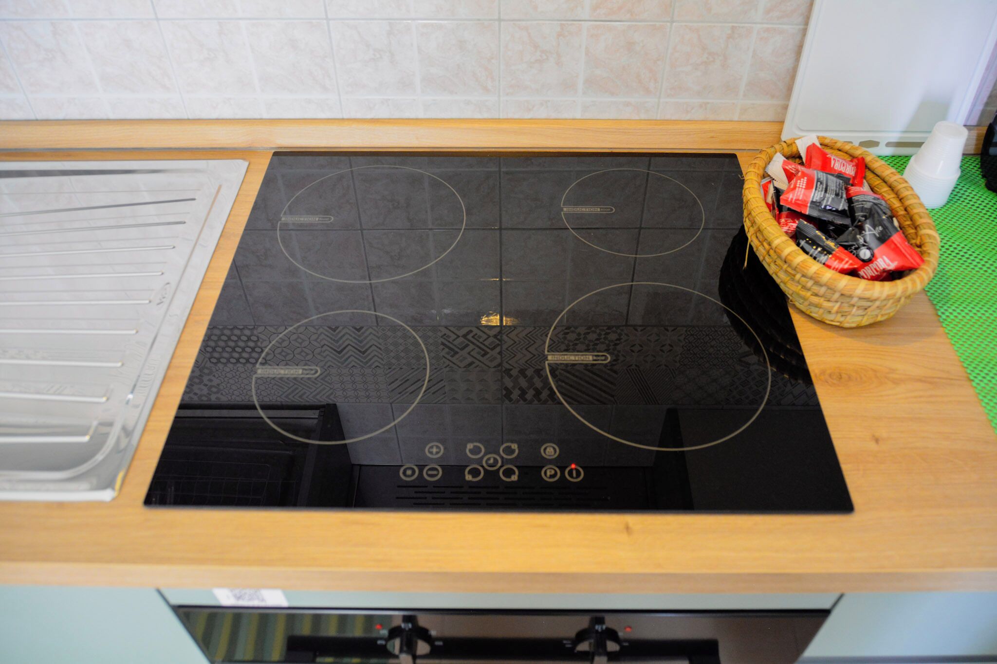 Een keuken met een zwart inductiekooktoestel, een houten aanrechtblad en een mand met rode en zwarte voorwerpen.