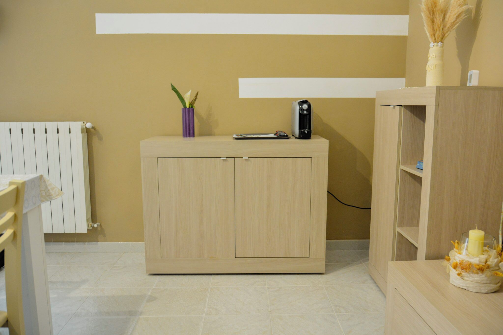 A room with a wooden cabinet, a radiator, and a shelf with a candle.