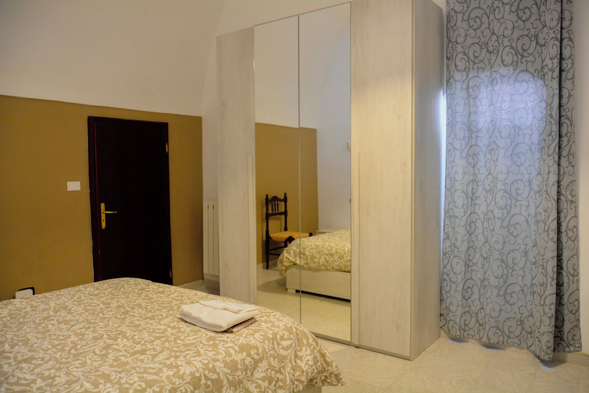 Habitació d'hotel amb llit, un armari, una cadira i una cortina.