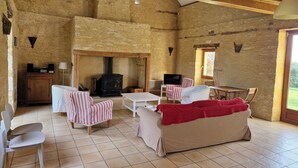 Habitación rústica con pared de piedra, vigas de madera, chimenea, televisor y una mesa de comedor con sillas.