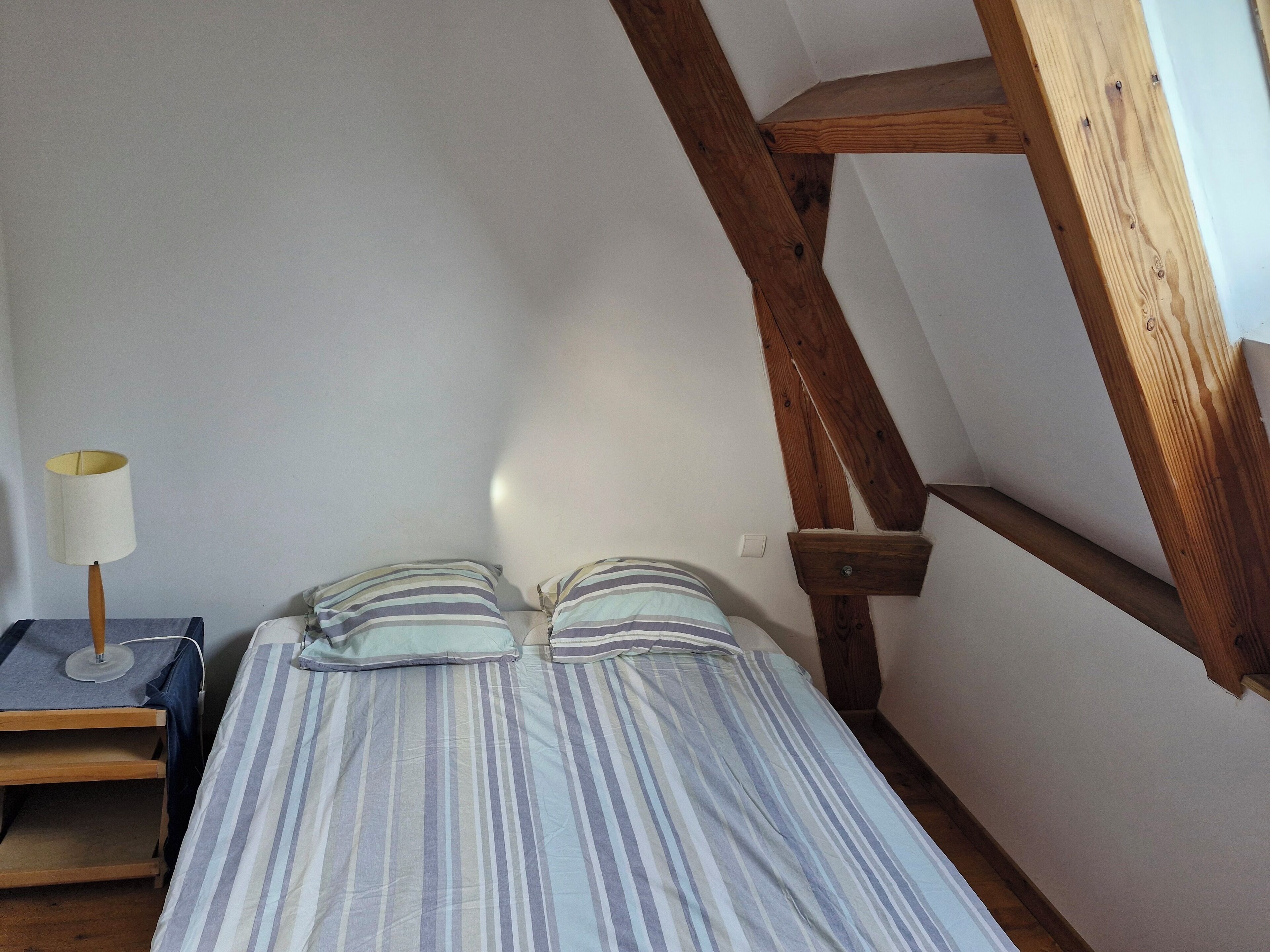 Una habitación pequeña y estrecha con una cama individual, una mesita de noche y una lámpara.