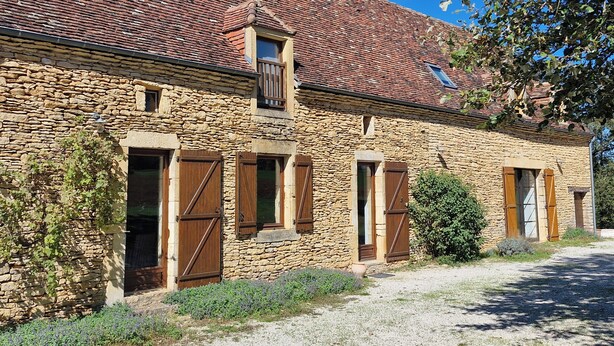 Un edificio de piedra con techo de tejas, contraventanas de madera y entrada de grava.
