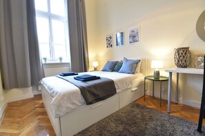 Ein Schlafzimmer mit Bett, Nachttischen, einem Fenster mit Vorhängen und Wandbildern.