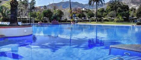 Una piscina con agua cristalina, rodeada de palmeras y montañas al fondo.