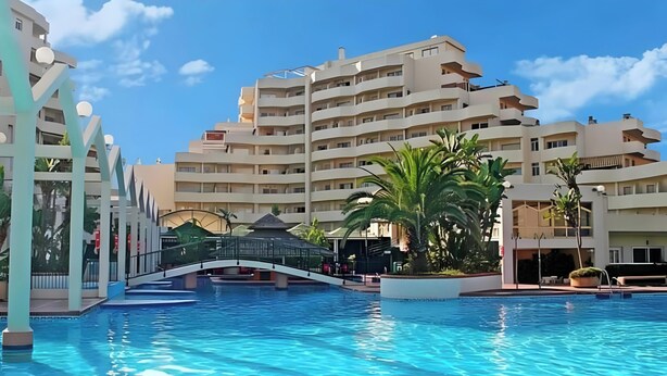 A swimming pool with a bridge, surrounded by multi-story buildings with balconies and a clear sky. - Vacation Home 'Relax Beach' with Shared Pool, Wi-Fi, and Air Conditioning (Benalmádena)