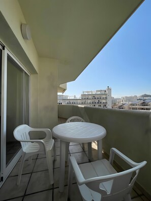 En balkon med et bord og stole, en skydedør samt udsigt til bygninger i baggrunden.