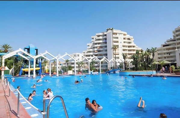 En swimmingpool med flere balkon niveauer, et vandrutsjebane og palmer.