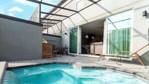 Une piscine avec un toboggan, un espace patio avec des chaises et une vue sur un bâtiment doté d’une porte en verre.