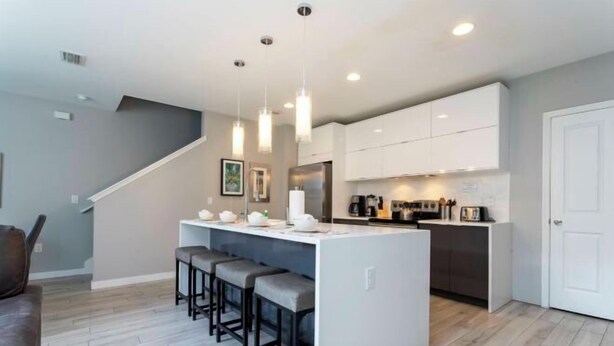 Une cuisine moderne avec des meubles blancs, un îlot central doté de tabourets et des luminaires suspendus.