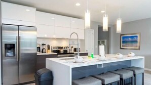 Une cuisine moderne dotée d’un îlot central, d’appareils électroménagers en acier inoxydable et de tabourets de bar.