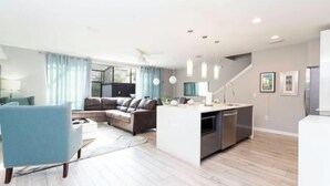 Un salon moderne avec un canapé, un fauteuil bleu, un îlot de cuisine et un escalier.