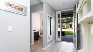 Un couloir doté d’un plancher de couleur claire, une porte donnant sur une salle de bain et une vue sur un jardin à l’extérieur.