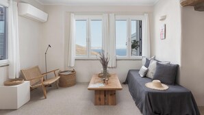 A cozy room with a view of the sea, a wooden table, a sofa, and a chair. - Azure 2, Morfes Luxury Apartments (Tinos)
