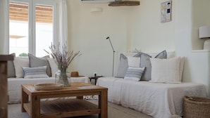 Une pièce chaleureuse avec une table basse en bois, deux lits blancs ornés d’oreillers à motifs, un vase contenant des plantes séchées et un climatiseur fixé au mur.