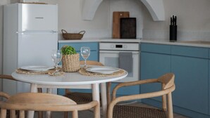 Une cuisine compacte avec un réfrigérateur blanc, des armoires bleues, une table à manger en bois avec quatre chaises et un petit îlot central agrémenté d’un panier et d’une plante.