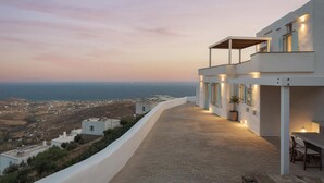 A modern building with a paved terrace overlooking a coastal landscape. - Green 1, Morfes Luxury Apartments (Tinos)
