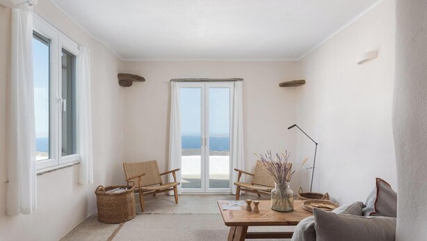 A spacious living room with a view of the sea, a balcony, wicker furniture, and a table with decorative items. - Green 3, Morfes Luxury Apartments (Tinos)